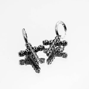 Image of The Skulled Cross Earrings displayed on a mirror. These unique earrings, crafted from Stainless Steel, embody a fusion of boldness and symbolism. Each pair represents a powerful blend of rebellion and mystique, making a captivating fashion statement. 